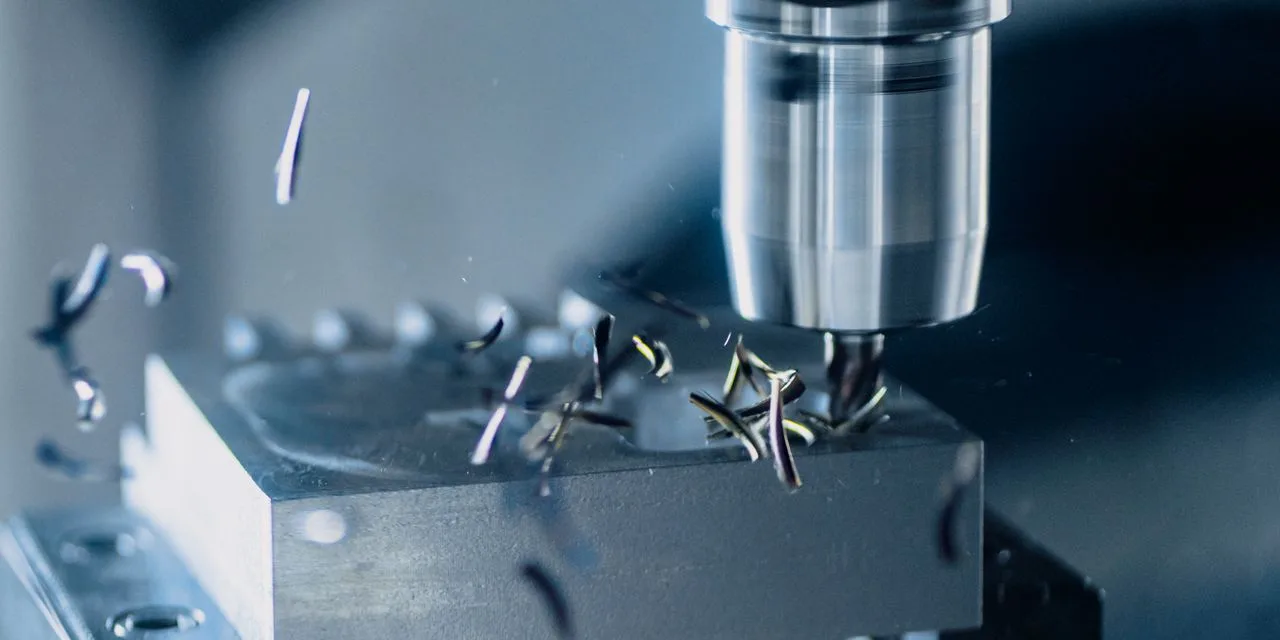 Ein kleines Aluminiumteil ist gespannt und wird gefräst, Späne fliegen zur Seite