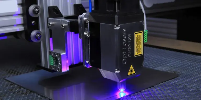 Ein Diodenlaser-Modul arbeitet über einer dunklen Metallplatte, blaues Licht trifft die Oberfläche