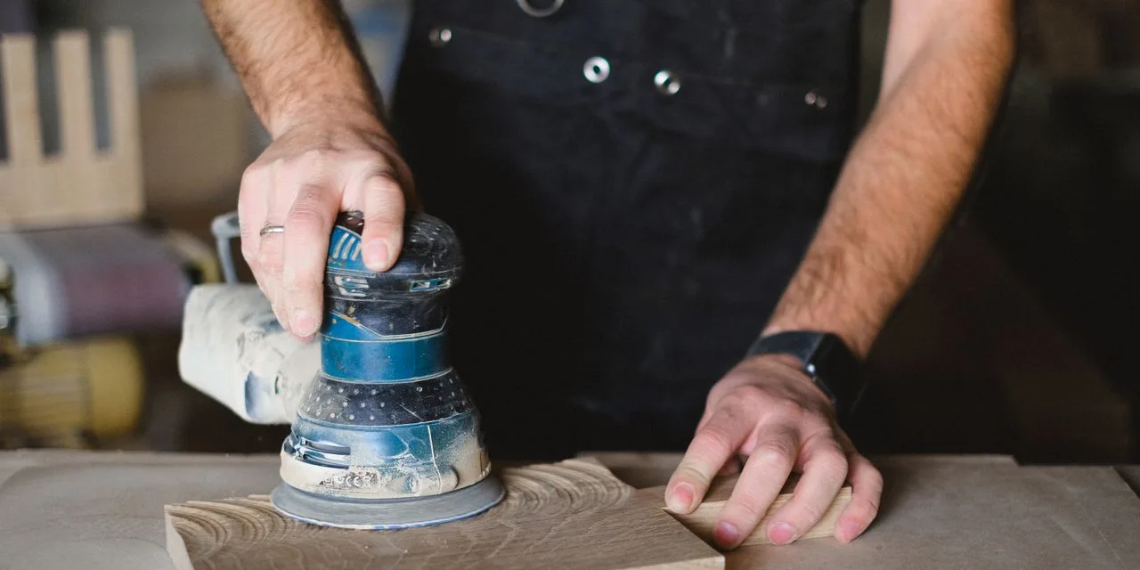 Metabo SXE 3125: leicht, aus Alu, mit Multi-Hole-Teller Ein Exzenterschleifer auf einer Holzfläche, die zweite Hand hält das Werkstück