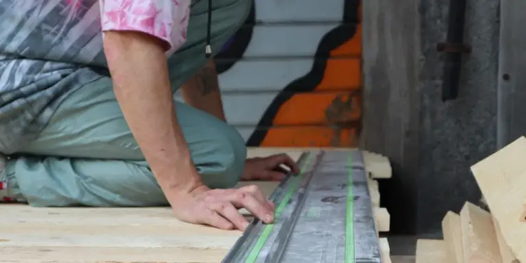 Eine Führungsschiene liegt auf einer Holzplatte, eine Hand hält sie an der Schnittlinie
