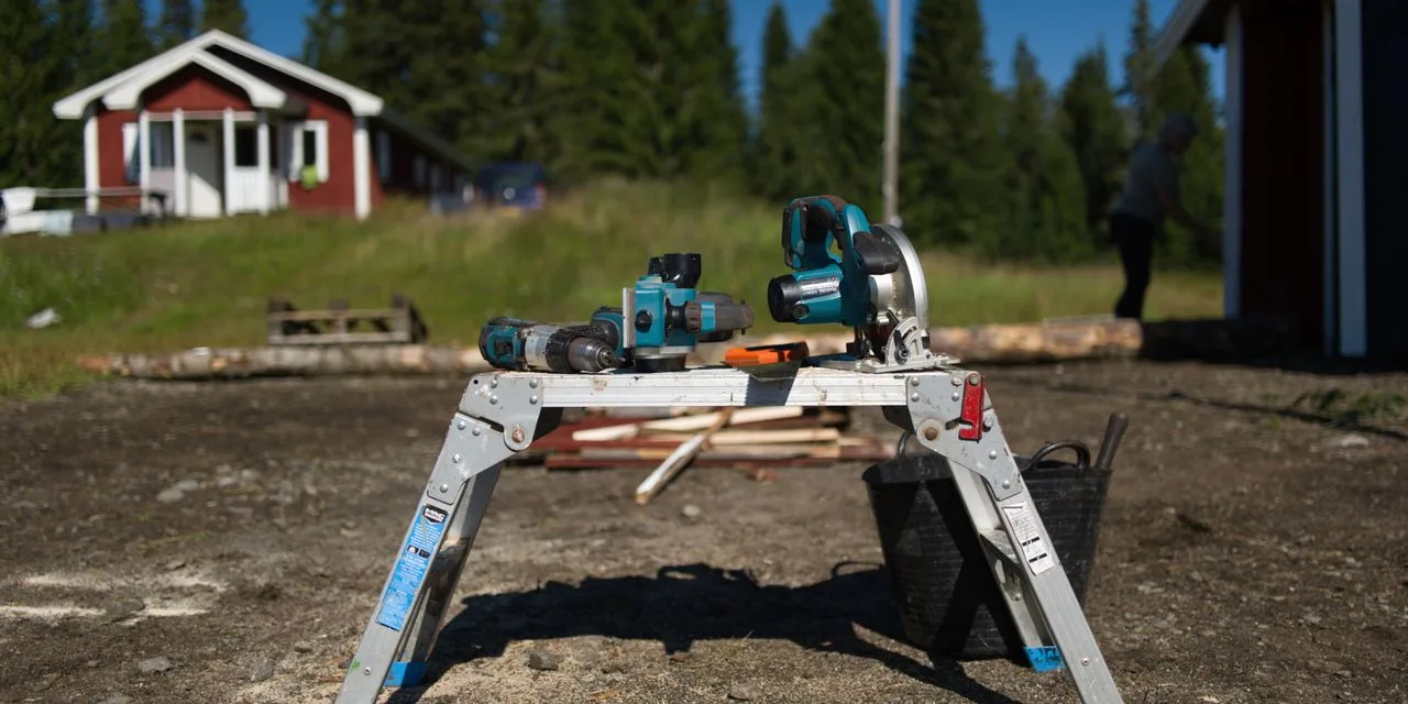 Eine Kappsäge steht auf einem Klappständer im Freien, dahinter ein rotes Holzhaus