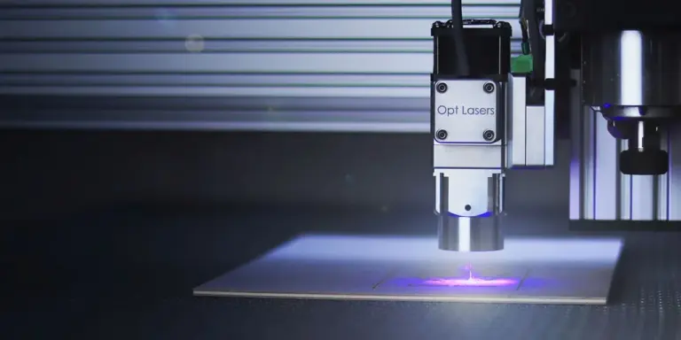 Ein Diodenlaser-Modul arbeitet über einer hellen Holzplatte, violettes Licht fällt auf das Werkstück