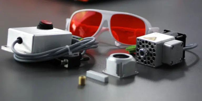 Eine rote Laserschutzbrille liegt vor einem Diodenlaser-Modul und seinem Zubehör