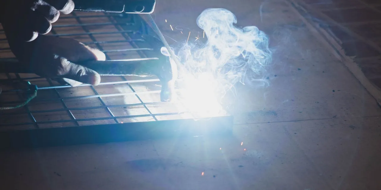 Stahlwerk Mini FLUX 120 ST: schweißen, wo Wind ist Geschweißt wird an einem Metallgitter, heller Lichtbogen und Rauch